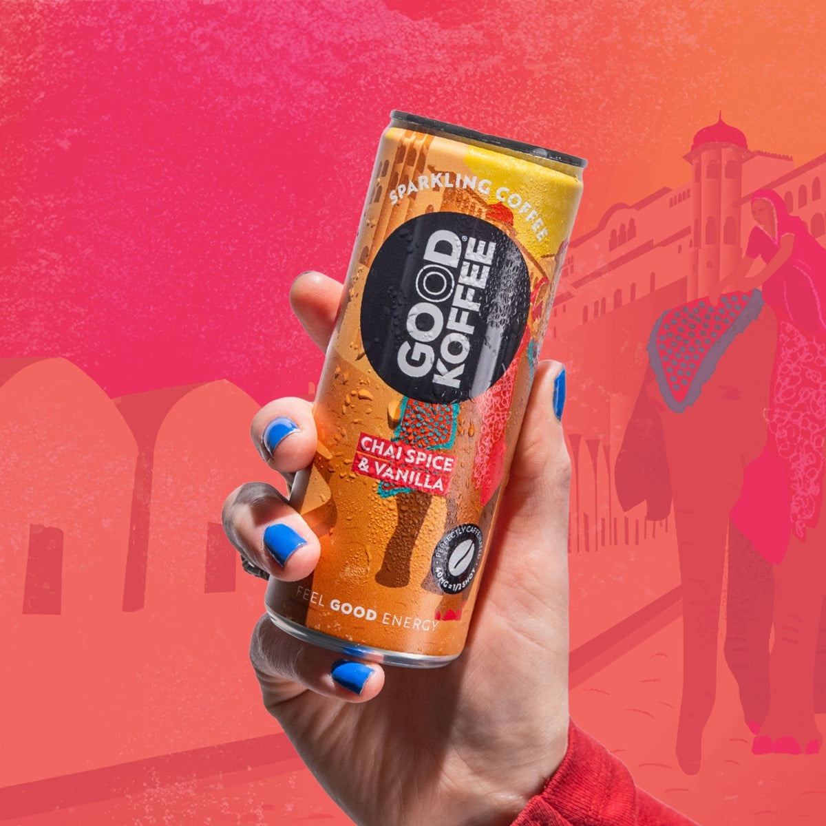 A hand with blue nail polish holds a can of Good Koffee Sparkling Coffee in Chai Spice & Vanilla flavor. The background is a stylized, warm-toned illustration of a street scene in shades of pink, orange, and red.