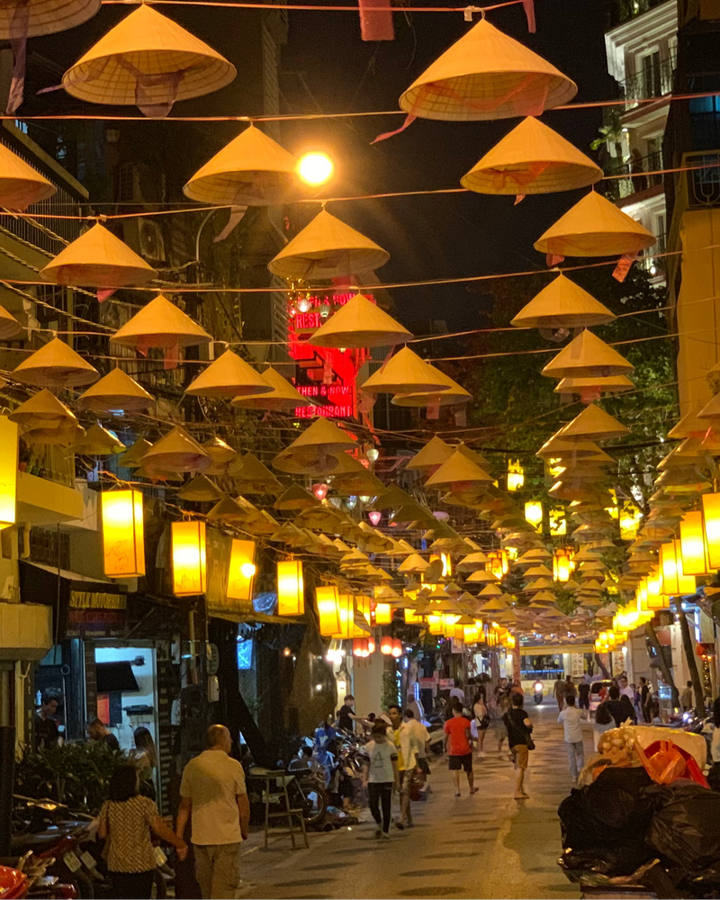 Nighttime street scene with traditional yellow hats and lanterns hanging above a busy street.