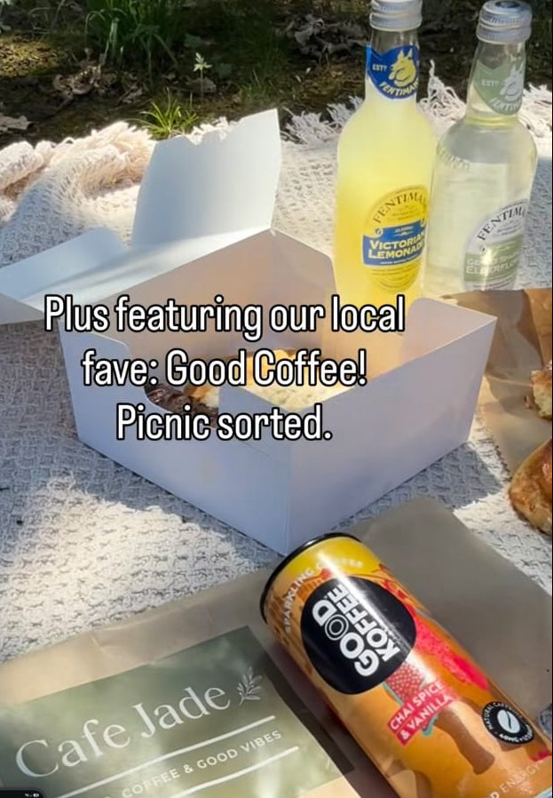 A social media post showing a picnic setup outdoors on a white blanket, featuring a white coffee box, two bottles of lemonade, a can of cold drink, and a green envelope labeled Cafe Jade.