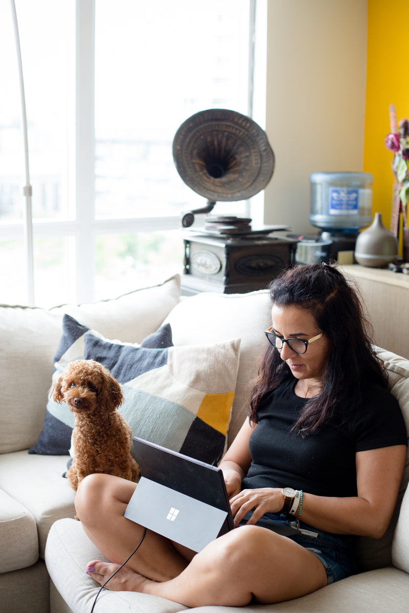 A woman sitting on a couch on their laptop next to a dog